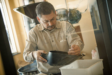 职场用具摄影照片_成熟男子将咖啡豆勺子用于咖啡馆的咖啡烘焙机