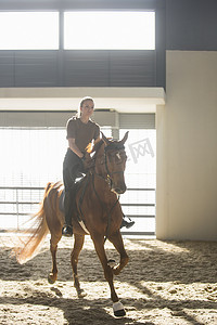 女子骑马摄影照片_一名女子在室内围场骑着栗色的马小跑