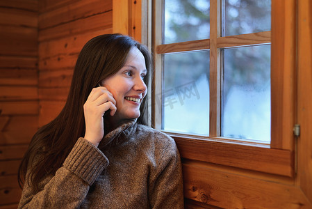 逃生窗户摄影照片_芬兰拉普兰一名年轻女子在智能手机上聊天看着窗外