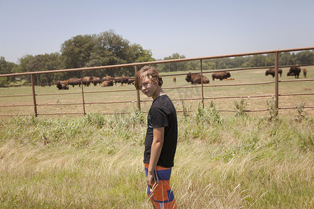 美国俄克拉何马州田野里水牛群旁边的十几岁男孩