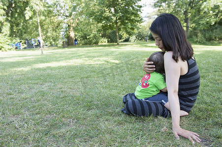 大家庭摄影照片_公园里成熟的母亲在大腿上拥抱幼子