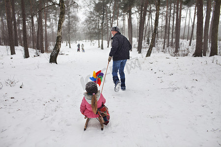 孩子动手摄影照片_父亲在雪地里拉着女儿穿着雪橇