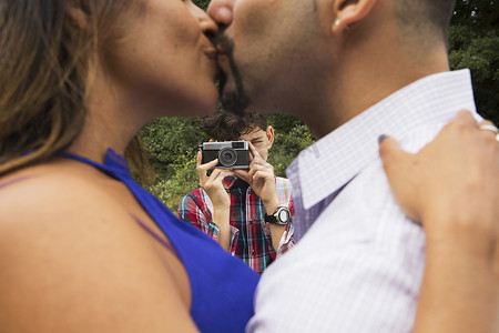 成年夫妇在户外接吻儿子用相机给他们拍照