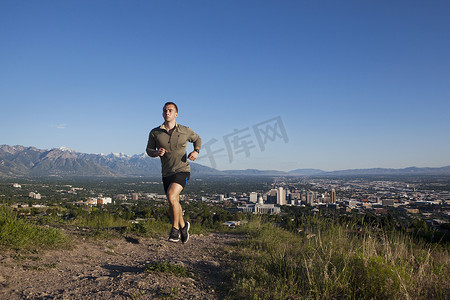 公路奔跑摄影照片_年轻的男性跑步者沿着山谷中城市上空的赛道奔跑
