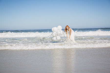 脚踝深埋大海的女人穿着白色连衣裙手持气球