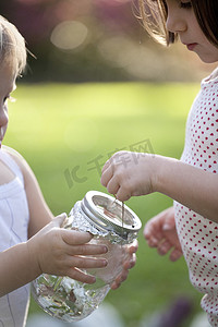 女孩和蹒跚学步的妹妹把绿色变色蜥蜴放进罐子里
