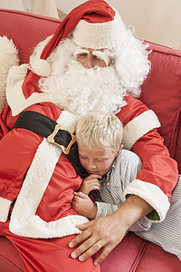 一名男子装扮成拥抱圣诞老人的男孩坐在沙发上