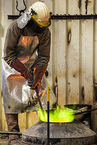 在青铜铸造厂使用绿色火焰熔炉工作的男性铸造工人