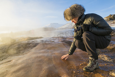 位于冰岛西南部山坡上的山谷中的一座间歇泉大间歇泉的女人正在触摸地面