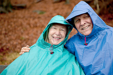 老年夫妇穿着防水服装坐在公园长凳上的肖像