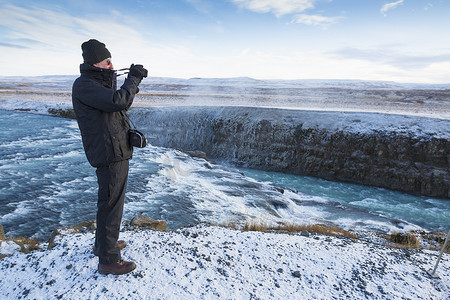一位资深男子在拍摄位于冰岛西南部河峡谷中的瀑布