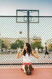 一名年轻女子靠在篮球场的栅栏上