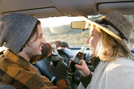 一对年轻夫妇在车里拿着瓶装可乐面带微笑