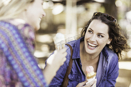 拿着冰淇淋摄影照片_拿着冰淇淋蛋卷的女人看着朋友微笑