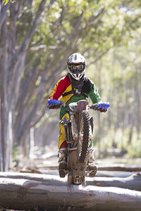 森林骑车摄影照片_年轻的男性越野摩托车手在森林原木上骑车