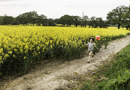 男孩拉着红色气球沿着黄色花田跑道奔跑