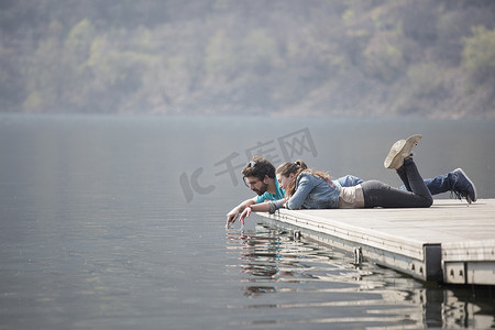 意大利皮埃蒙特韦尔巴尼亚的梅尔戈佐湖一对年轻夫妇躺在码头上蘸手指