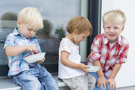 一个蹒跚学步的女孩子和两个弟弟在院子里吃着几碗覆盆子
