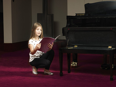 蹲在舞台上朗读钢琴乐谱的女孩