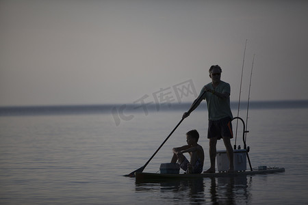 美国密歇根州奥特林湾苏必利尔湖剪影男子和十几岁的儿子在冲浪板上钓鱼