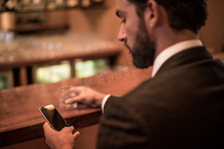 一名商人在酒店酒吧阅读智能手机短信
