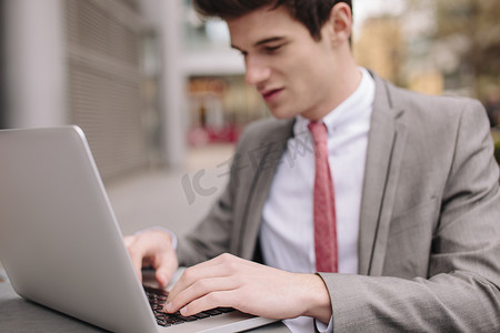 路边咖啡厅摄影照片_一名年轻的城市商人在路边咖啡馆用笔记本电脑打字