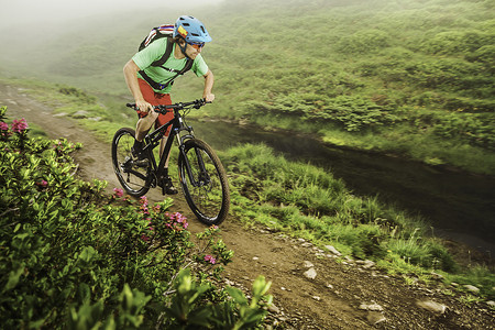 年轻的男性山地自行车手在溪流旁骑自行车
