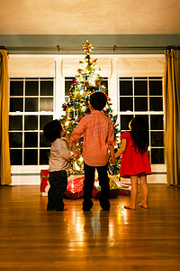 女孩和两兄弟在圣诞树前手牵手的背影