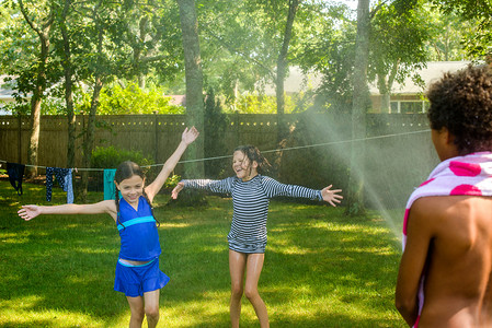 三个孩子用花园水管在花园里玩耍