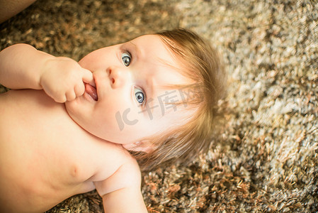 女婴躺在地毯上手指夹在嘴里看向别处的高空视角