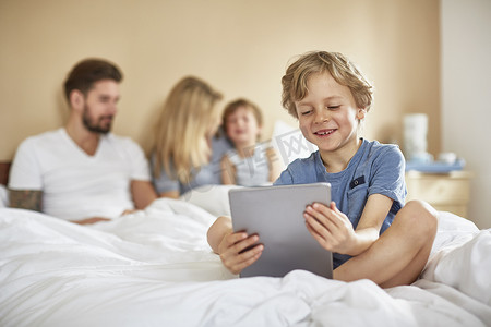 躺在父母床上的男孩用数字平板电脑微笑