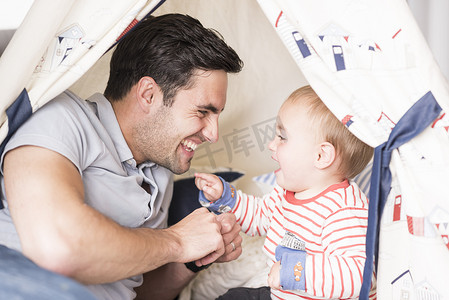 父亲和儿子坐在室内的帐篷里玩耍一起大笑