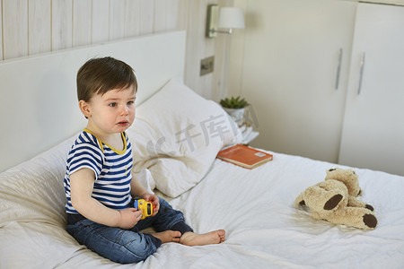 玩具车摄影照片_悲伤的男婴坐在床上抱着玩具车看着别处