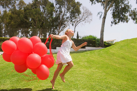 带着红色气球跳跃的年轻女孩