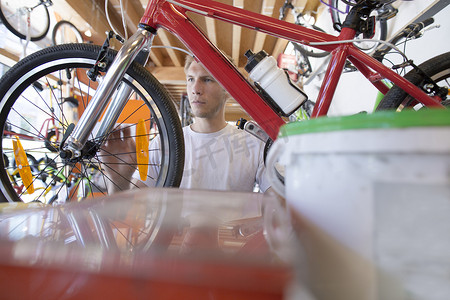 力学摄影照片_修理店里的中年男子透过自行车车架看