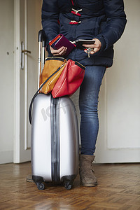 妇女站在门口提着打包的手提箱检查手提包中的护照