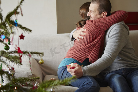 圣诞节一对情侣手持圣诞礼物在沙发上拥抱