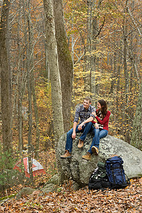 一对年轻夫妇坐在森林里的巨石上