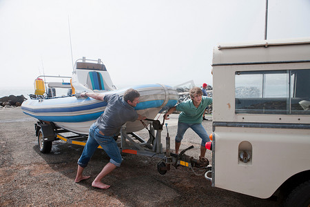 小艇摄影照片_两名年轻男子将小艇拖车固定在车辆上