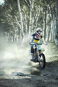 森林骑车摄影照片_年轻的男子越野摩托车手在森林的水坑里骑车