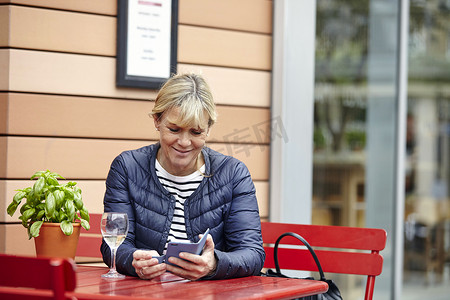 成熟女性在路边咖啡馆阅读智能手机短信
