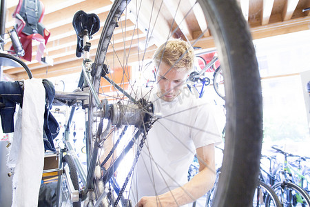 力学摄影照片_中年男子修理自行车透过轮子观看
