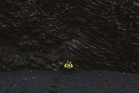 冰岛一名中年男子坐在柱状玄武岩岩壁下