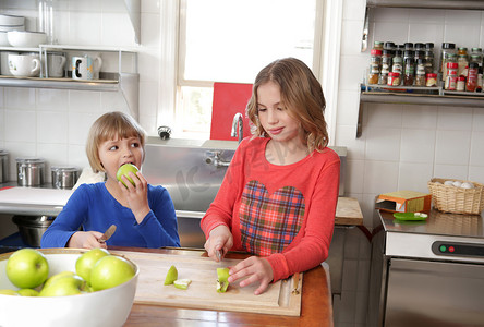 两个在柜台摄影照片_两个年轻女孩在厨房里切苹果
