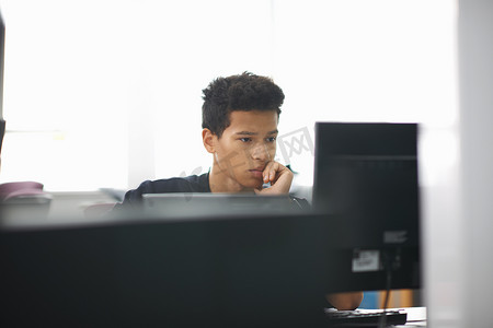 年轻的男大学生坐在书桌前看电脑
