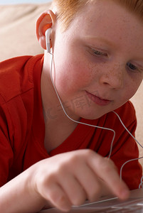 戴着耳机的男孩在沙发上使用笔记本电脑