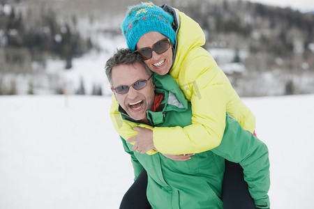 成熟的男人在雪地里背着年轻的女人笑着