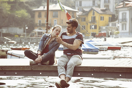 在意大利皮埃蒙特韦尔巴尼亚的梅尔戈佐湖一对夫妇坐在码头上分享蛋卷冰淇淋