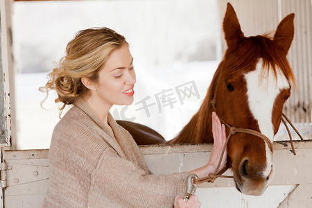 农用地摄影照片_在马厩里照看马的年轻女子