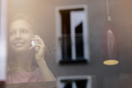 街边聊天摄影照片_一名年轻女子在咖啡馆橱窗边用智能手机聊天
